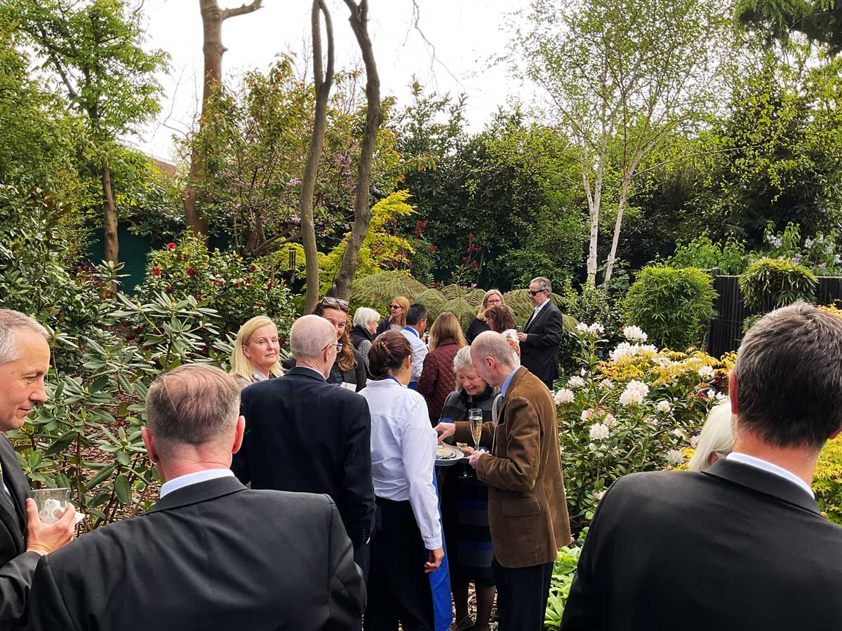 Mourners at a wake, paying their respects to a loved one in the peaceful discretion of Rosy's secret garden.