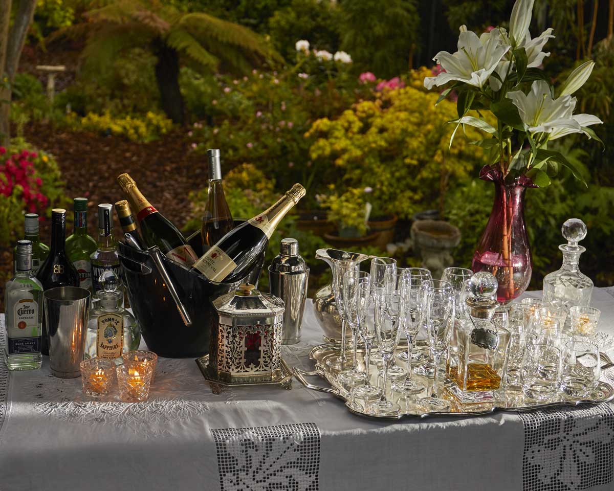 Beautiful bar set up with bucket full champagne bottles and glasses on the right, and the beautiful blooming garden in the background.