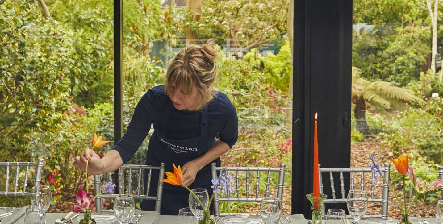 Simone, Rosy's florist, arranging flowers on a beautifully set table with the garden behind it.