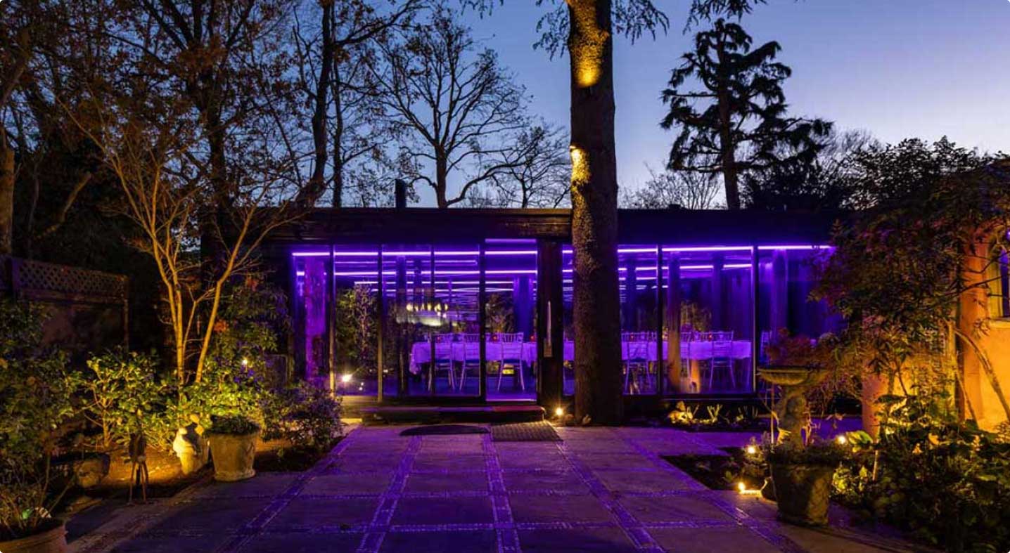 The Pailion at night, surrounded by trees, with atmospheric purple lighting inside.