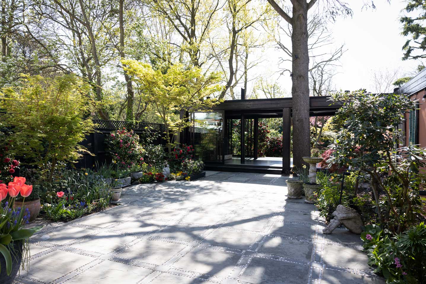 The view that greets visitors upon entering: he patio lined with blooming bushes, and the pavilion at the bottom, surrounded by majestic trees.
